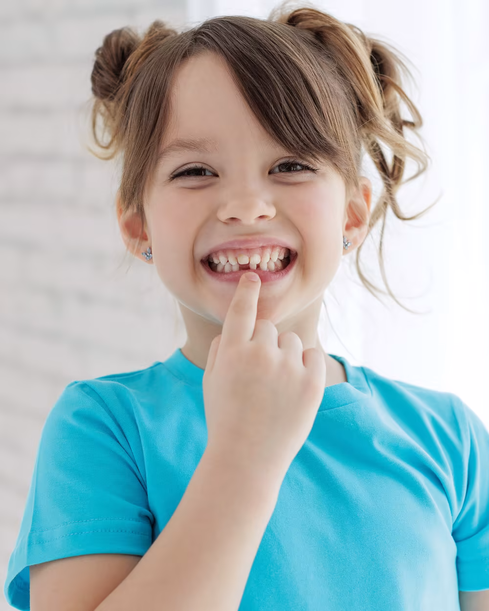 Smiling girl pointing to her smile with a missing front tooth